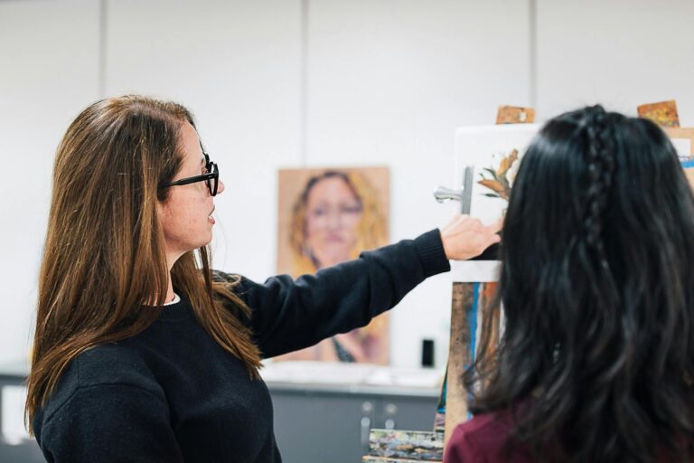 Female teacher instructing a student at a painting easel.